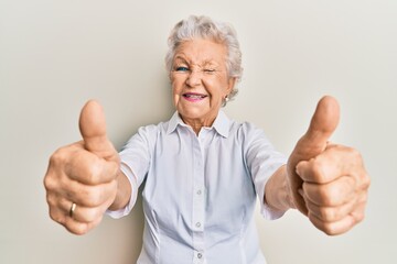 Senior grey-haired woman doing thumbs up positive gesture winking looking at the camera with sexy...