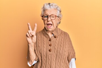 Senior grey-haired woman wearing casual clothes and glasses smiling with happy face winking at the...