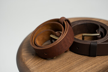 Two brown leather men's belts with bronze clasp on wooden chair with a white background. Handmade leather belt.