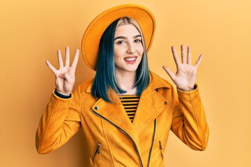 Young modern girl wearing yellow hat and leather jacket showing and pointing up with fingers number...