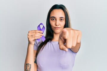 Young hispanic woman holding purple ribbon awareness pointing with finger to the camera and to you,...