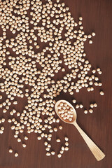 Fototapeta premium Raw chickpeas in a wooden spoon scattered on a wooden background. Top view. Copy, empty space for text
