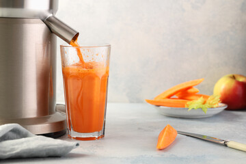 Carrot juice is poured from an electric juicer into a glass beaker.Delicious drink rich in vitamins and carotene.