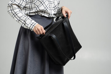 Small black leather bag in a woman's hand on a white background. Shoulder handbag. Woman in a white plaid shirt and black jeans and with a black handbag. Style, retro, fashion, vintage and elegance.