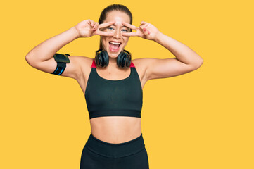 Fototapeta na wymiar Beautiful blonde woman wearing gym clothes and using headphones doing peace symbol with fingers over face, smiling cheerful showing victory