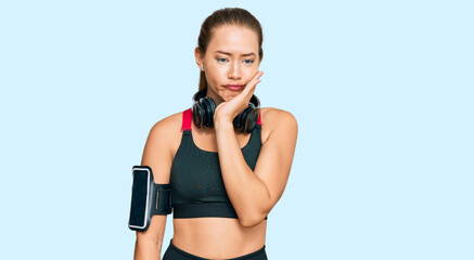 Beautiful blonde woman wearing gym clothes and using headphones thinking looking tired and bored with depression problems with crossed arms.