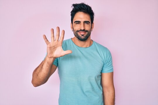 Handsome hispanic man with beard wearing casual clothes showing and pointing up with fingers number five while smiling confident and happy.