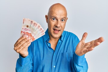 Middle age bald man holding 10 colombian pesos banknotes celebrating achievement with happy smile...