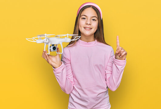 Beautiful brunette little girl using drone surprised with an idea or question pointing finger with happy face, number one