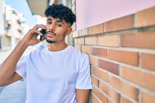 Young arab man with serious expression talking on the smartphone leaning on the wall.