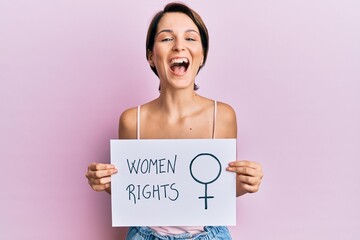 Young brunette woman with short hair holding woman rights banner smiling and laughing hard out loud...