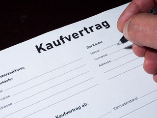  Nahaufnahme von einem Finger mit Kugelschreiber und Kaufvertrag.