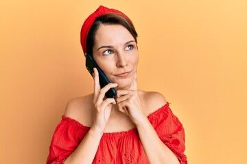 Young brunette woman with short hair having conversation talking on the smartphone serious face thinking about question with hand on chin, thoughtful about confusing idea