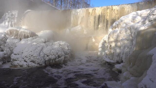 Helsinki, Finland - February 18, 2021: Water pours over the dam in the mouth of Vantaa River at the frozen Vanhankaupunginkoski rapids (Vanhankaupunginkosken putous) on extremely cold day in February 