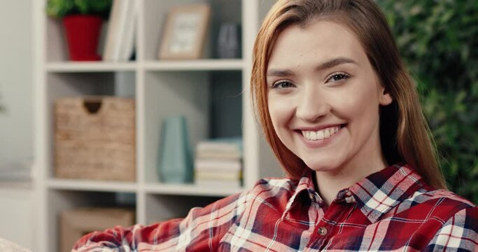 Portrait of young beautiful girl in plaid shirt is resting at home on couch and smiling looks at camera.