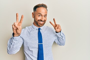 Handsome middle age man wearing business shirt and tie smiling looking to the camera showing fingers doing victory sign. number two.