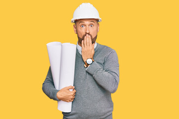 Handsome middle age man holding paper blueprints covering mouth with hand, shocked and afraid for...