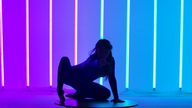 An attractive woman performs a handstand, moves her legs and splits them into a split. Gymnast in the studio against the background of pink and blue lights. Silhouette. Slow motion. Close up.