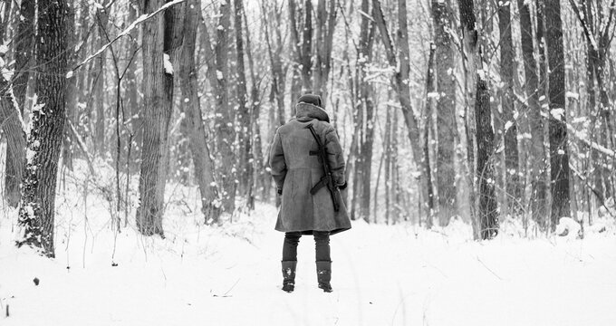 Soviet soldier in coat is standing with a gun in the winter forest 