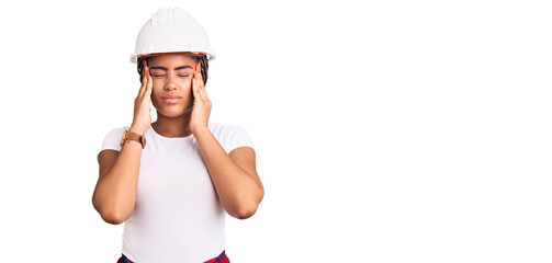 Young african american woman with braids wearing hardhat and builder clothes suffering from headache desperate and stressed because pain and migraine. hands on head.