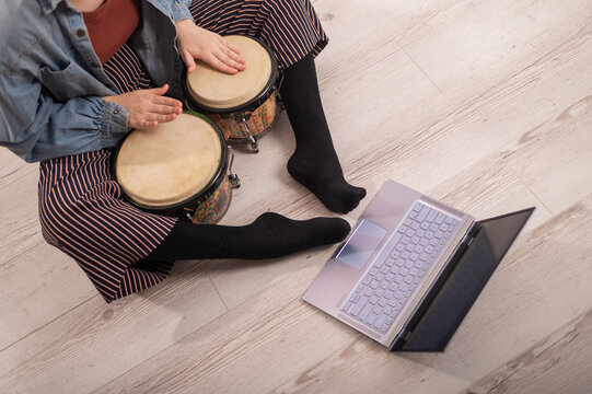 A faceless woman sits on the floor at home and watches educational videos of playing mini bongs. Girl remotely learns to play traditional ethnic drums.