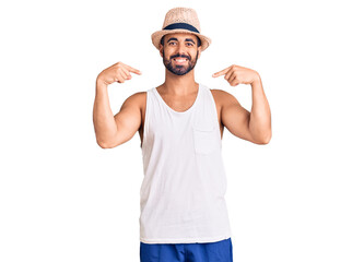 Young hispanic man wearing casual summer hat looking confident with smile on face, pointing oneself...