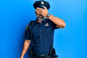 Middle age handsome man wearing police uniform covering eyes with hand, looking serious and sad. sightless, hiding and rejection concept