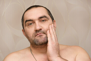 Obraz premium 40-year-old bearded man touches stubble on face with hand. Time to shave your beard. Male facial care concept at home