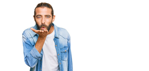 Attractive man with long hair and beard wearing casual denim jacket looking at the camera blowing a kiss with hand on air being lovely and sexy. love expression.