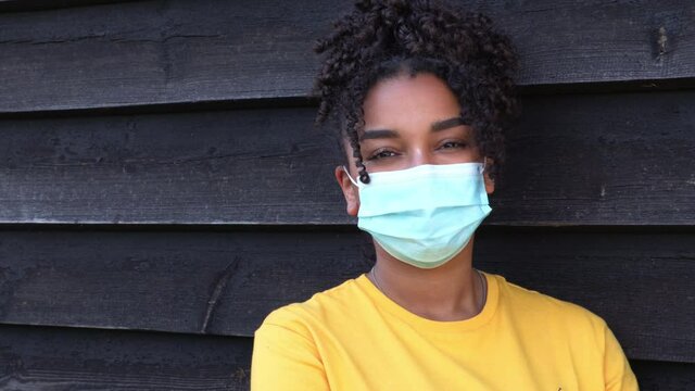 Beautiful mixed race African American girl biracial teenager teen young woman outside wearing a face mask during COVID-19 Coronavirus pandemic