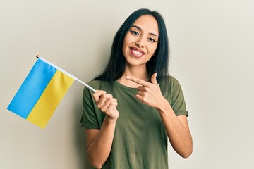 Young hispanic girl wearing ukraine flag smiling happy pointing with hand and finger