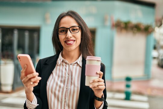Young hispanic businesswoman using smartphone drinking coffee at the city.