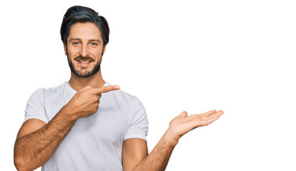 Young hispanic man wearing casual white t shirt amazed and smiling to the camera while presenting with hand and pointing with finger.