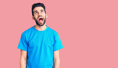 Young handsome man with beard wearing casual t-shirt angry and mad screaming frustrated and furious, shouting with anger. rage and aggressive concept.