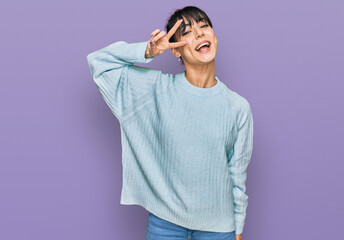 Young hispanic woman wearing casual clothes doing peace symbol with fingers over face, smiling...