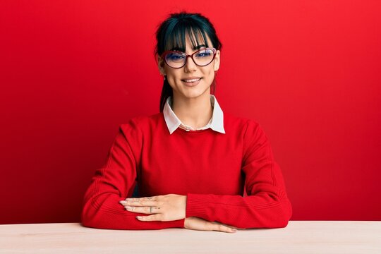 Young brunette woman with bangs wearing glasses sitting on the table with a happy and cool smile on face. lucky person.