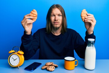 Handsome caucasian man with long hair eating croissant for breakfast clueless and confused...