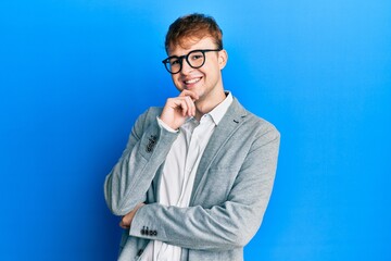 Young caucasian man wearing elegant clothes and glasses looking confident at the camera with smile with crossed arms and hand raised on chin. thinking positive.