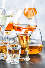 Strong alcoholic drinks in glasses in assortment: vodka, cognac, tequila, brandy and whiskey, grappa, liqueur, vermouth, tincture, rum. Gray bar counter with copy space