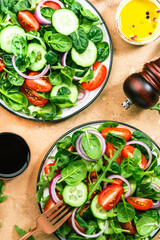 Spring green salad with spinach, cherry tomatoes, corn salad and red onion. Healthy food concept. Beige stone table. Top view. Copy space