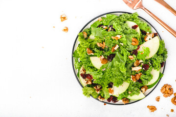 Kale salad with dried cranberry, green apples and walnuts. Healthy vegan food, top view, grey kitchen table background