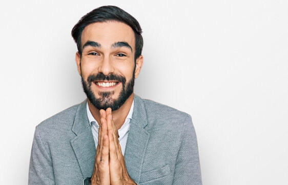 Young hispanic man wearing business clothes praying with hands together asking for forgiveness smiling confident.