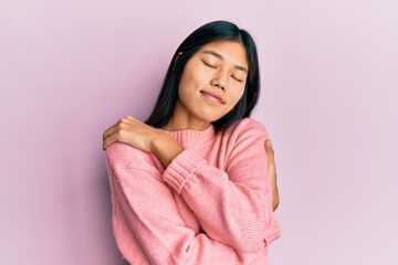 Young chinese woman wearing casual clothes hugging oneself happy and positive, smiling confident. self love and self care