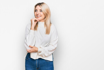 Young caucasian woman wearing casual winter sweater with hand on chin thinking about question, pensive expression. smiling and thoughtful face. doubt concept.