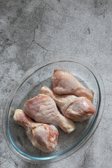 Frozen raw chicken defrosting in a glass dish.  On a concrete background