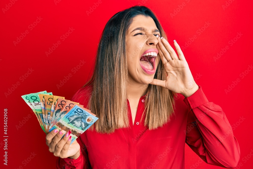 Sticker Beautiful brunette woman holding australian dollars shouting and screaming loud to side with hand on mouth. communication concept.