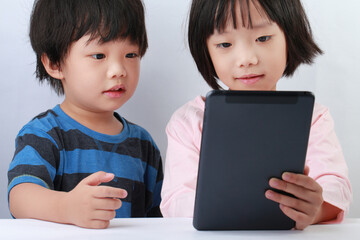 Portrait of cute Asian sibling using a tablet on the desk