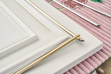 Gluing elegant golden molding decorative strip on furniture white facade panel in classical style...