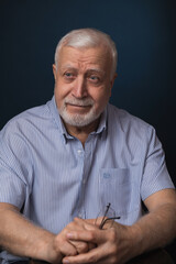 elderly handsome charismatic man sitting with glasses in hand and smiling, studio, dark background, portrait