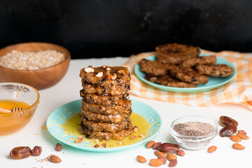 homemade oatmeal banana pancakes with chia seeds, almonds, prunes and dates, drizzled with honey and crushed nuts on a dark background. diet breakfast is healthy for the figure .